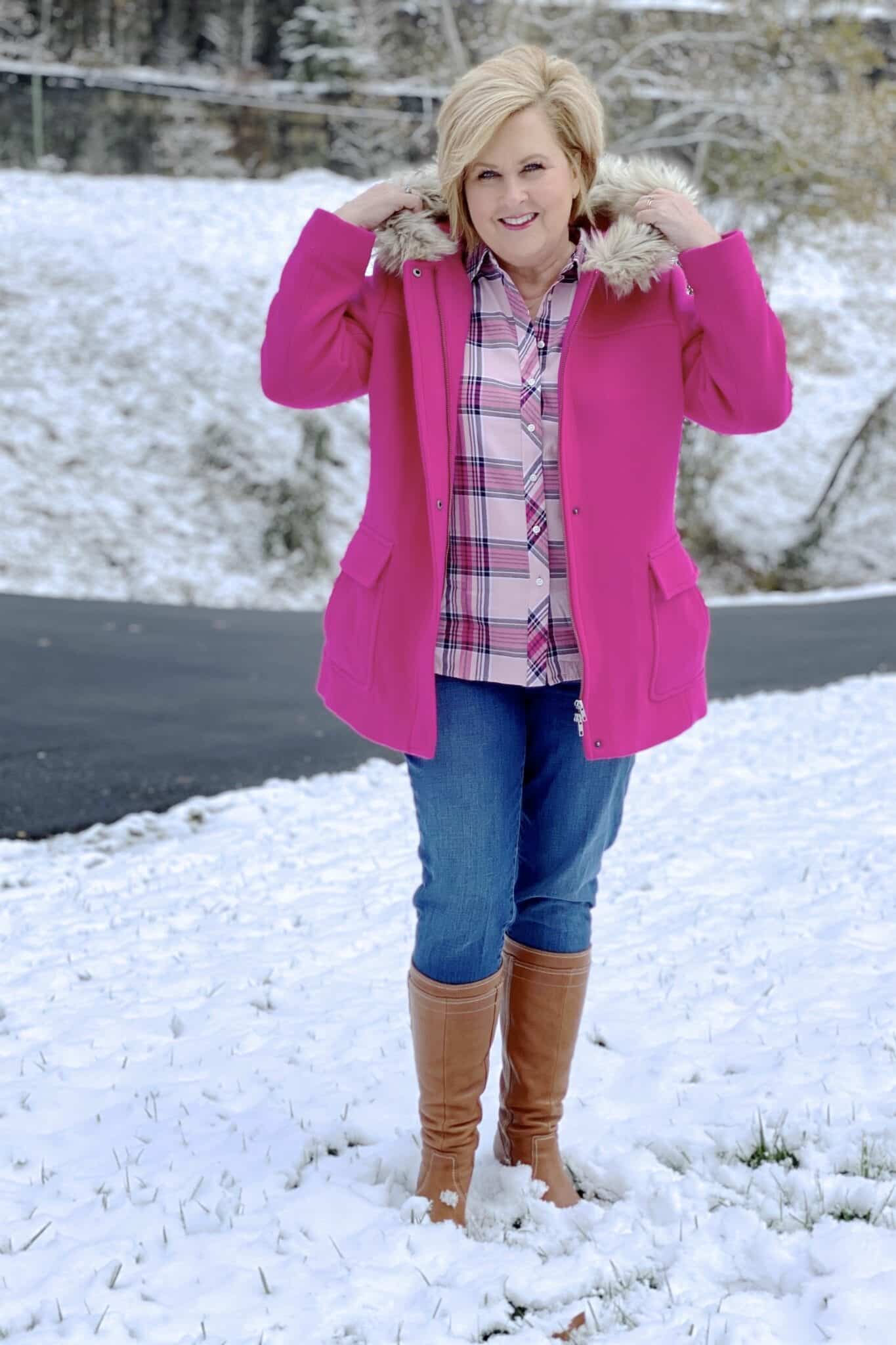 A blonde woman in snow with a bright pink coat with a faux fur hood