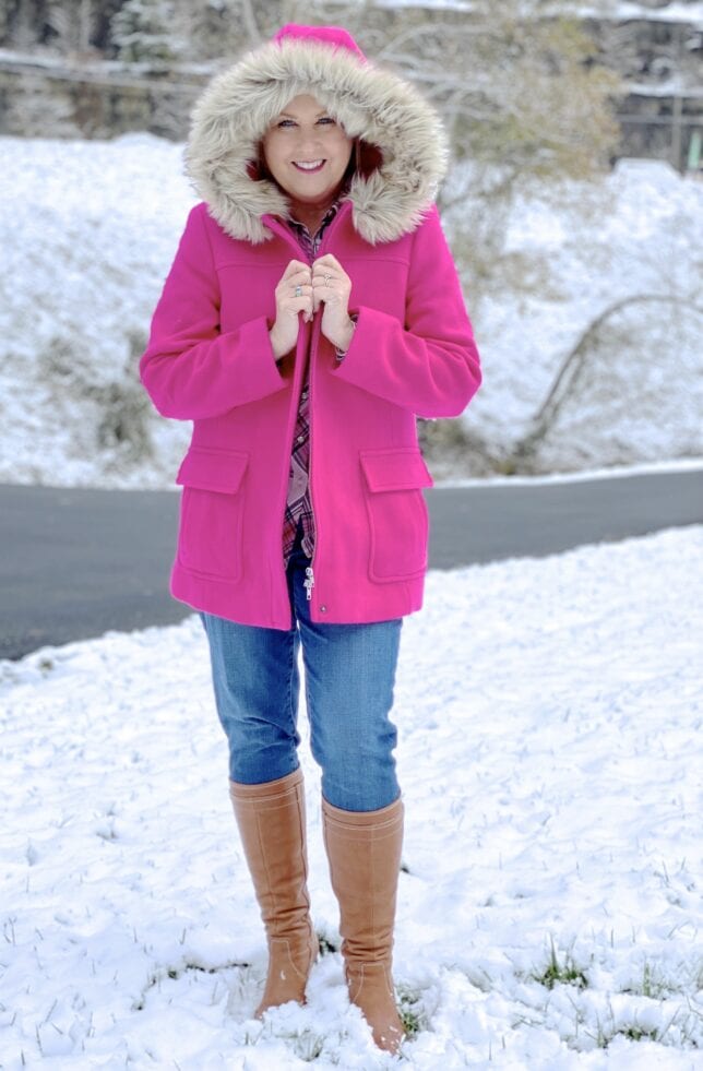 A blonde woman in the snow with a bright pink wool coat with a faux fur hood