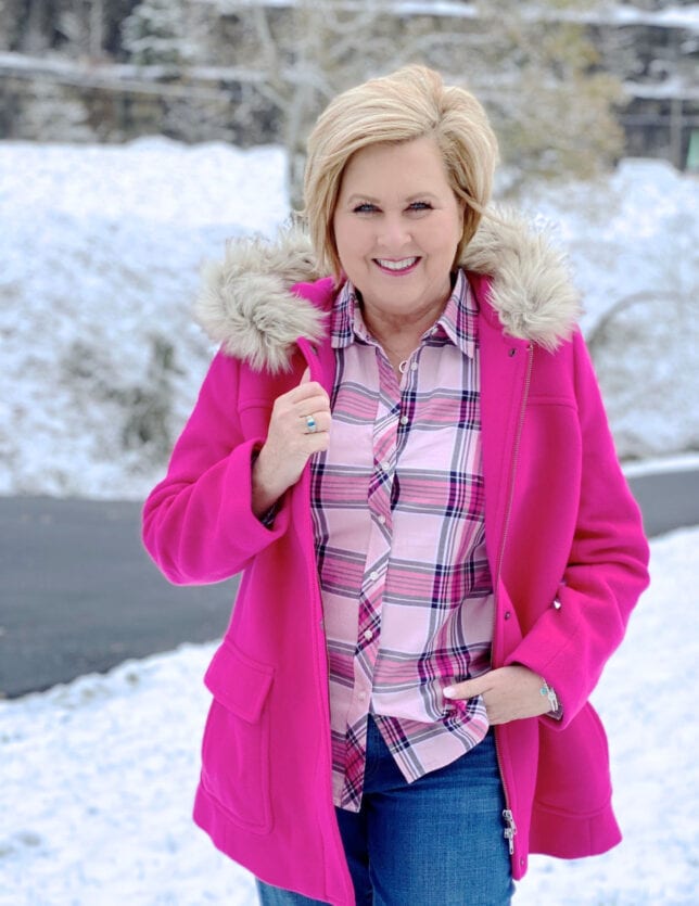 A blonde woman in the snow with a bright pink coat with a faux fur hood