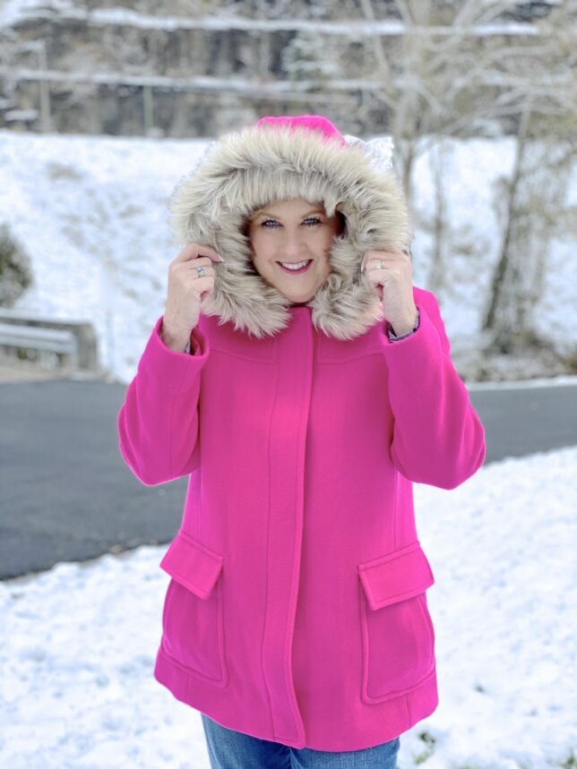 A woman in the snow with a bright pink coat with a faux fur hood