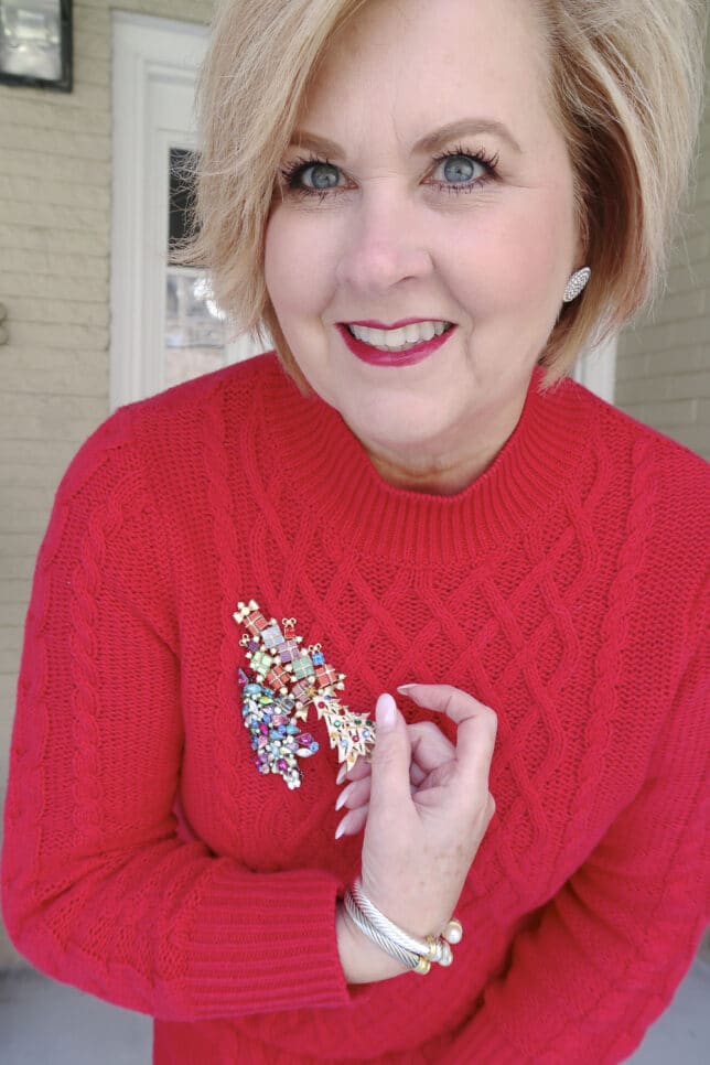 Fashion Blogger 50 is not old wearing a red sweater dress showing vintage Christmas tree pins