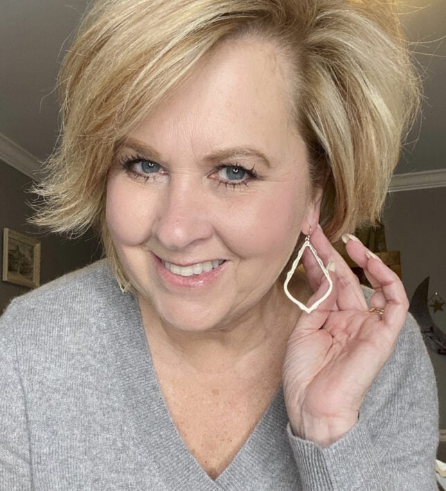 Fashion Blogger 50 Is Not Old holds a try on session and show a gold drop earring from Kendra Scott