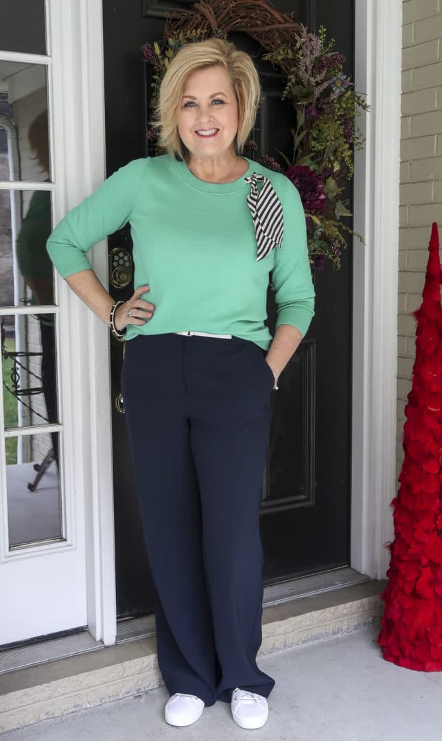 Fashion Blogger 50 Is Not Old wearing a light Jade sweater with a striped scarf with navy wide leg pants.