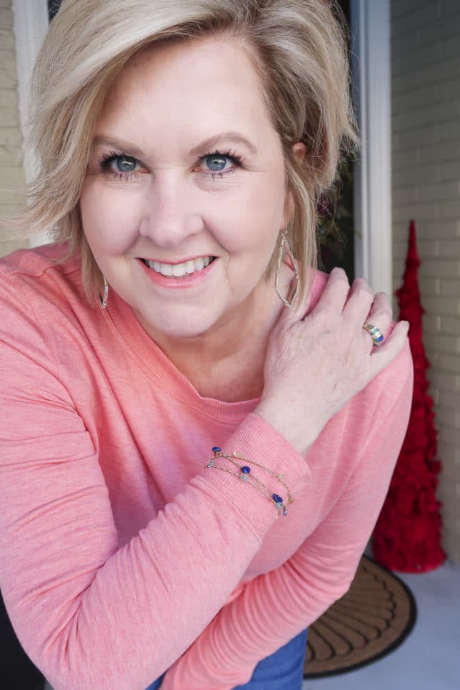 Fashion Blogger 50 Is Not Old is wearing a soft rose/coral tunic top and a pair of gold earrings