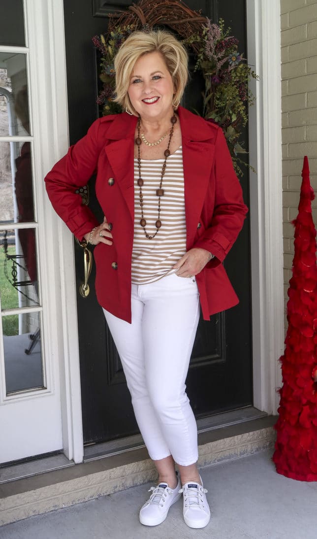 Fashion Blogger 50 Is Not Old is wearing her rainy weather style of a pair of white jeans with a tan striped top and a red trench coat