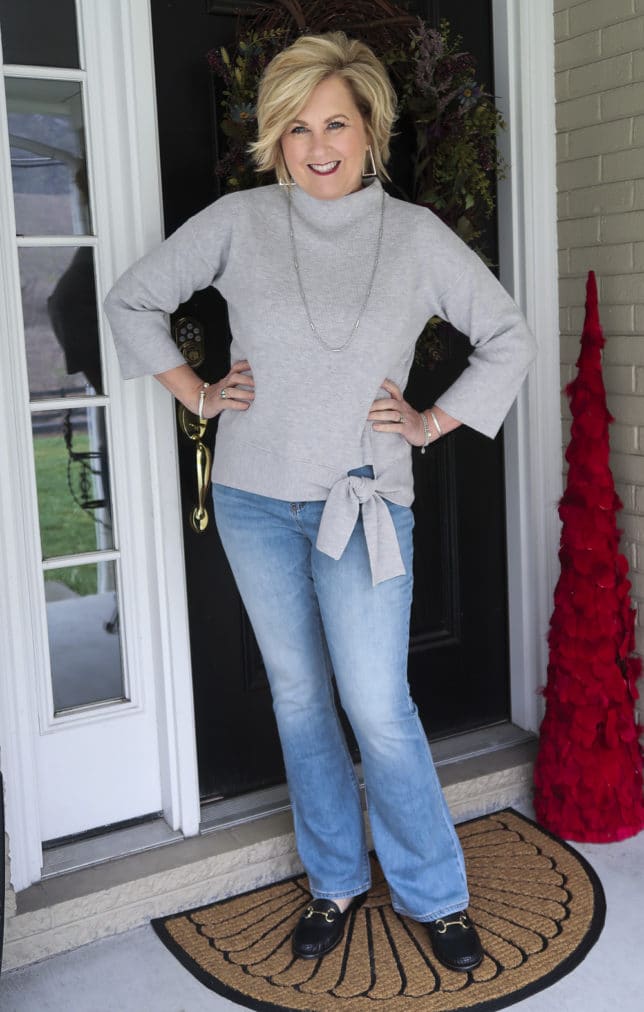 Fashion Blogger 50 Is Not Old wearing a gray side-tie sweater and a pair of high-waist jeans from Chico's with black mule loafers