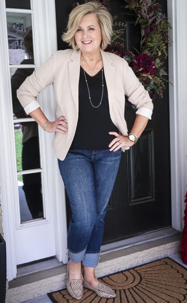 Fashion Blogger 50 Is Not Old in a taupe knit blazer, a black v-neck t-shirt, and cuffed jeans