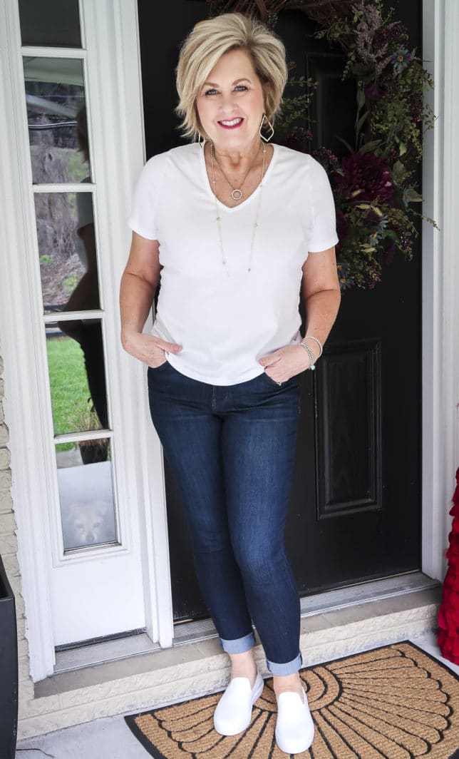 Fashion Blogger 50 Is Not Old is wearing a white v-neck t-shirt, dark wash jeggings, and white slip-on slippers