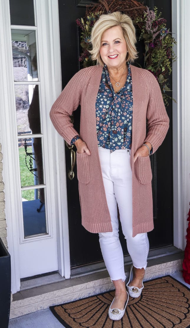Fashion Blogger 50 Is Not Old is wearing white jeans before Memorial Day with a blue floral blouse, a pink chunky knit cardigan, and white loafers
