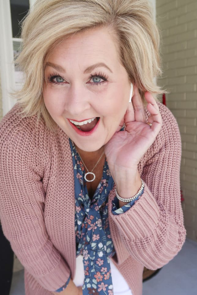 Fashion Blogger 50 Is Not Old is wearing a blue floral blouse and a chunky knit cardigan with Airpods