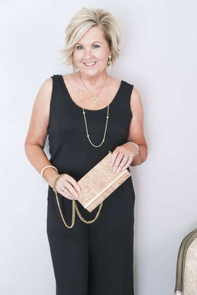 50 Is Not Old is wearing a black sleeveless wide leg ankle length jumper with a cork clutch handbag