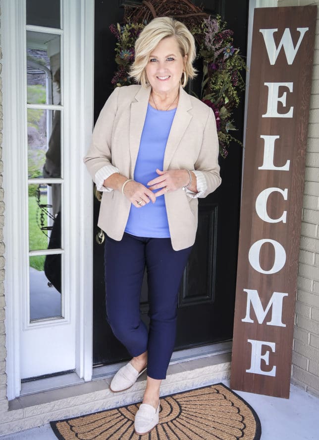 Fashion Blogger 50 Is Not Old is wearing a periwinkle blue t-shirt with navy ankle pants, a beige blazer, and linen looking mules