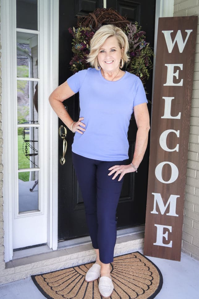 Fashion Blogger 50 Is Not Old is wearing a periwinkle blue t-shirt with navy ankle pants, and linen looking mules