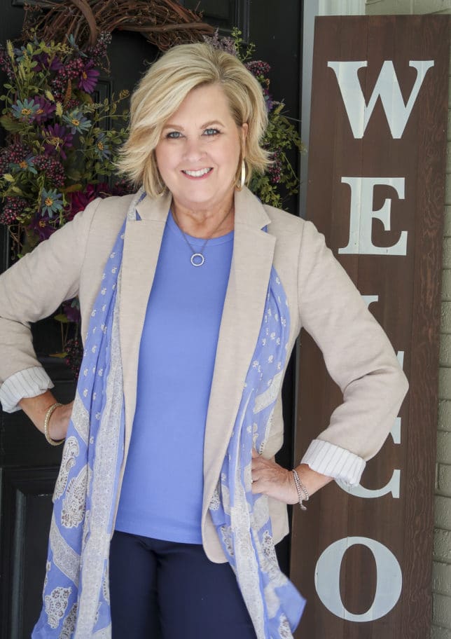 Fashion Blogger 50 Is Not Old is wearing a periwinkle blue t-shirt with navy ankle pants, a beige blazer, a long blue scarf, and gold jewelry from Kendra Scott