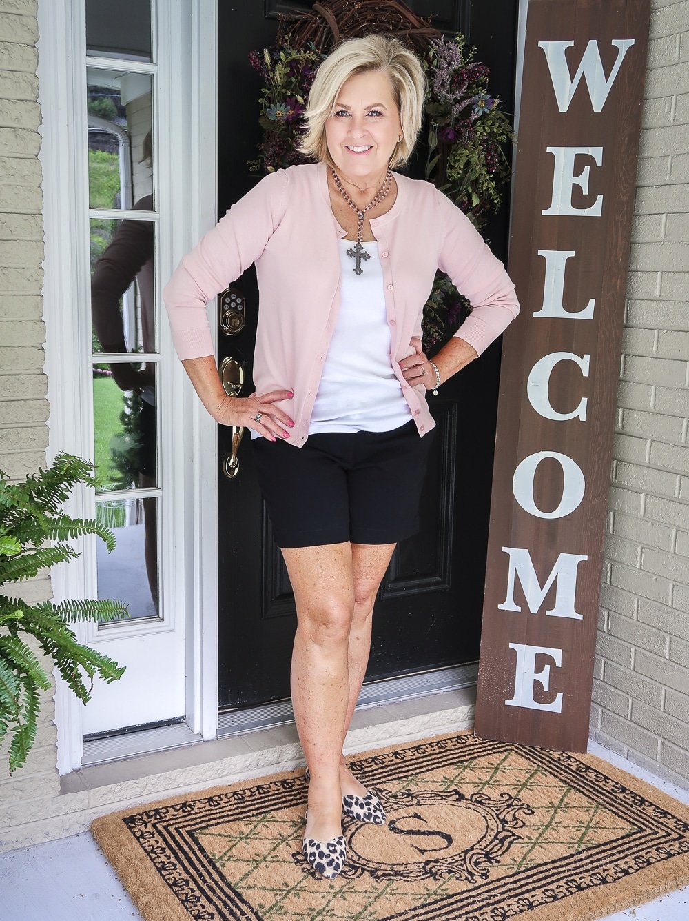 Fashion Blogger 50 Is Not Old is wearing a soft pastel pink cardigan from Walmart, a white tank top, black 7" shorts from Loft, and leopard print flats from Old Navy