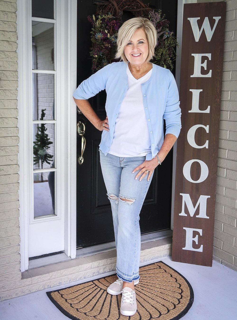 Fashion Blogger 50 Is Not Old is wearing a light blue cardigan and a white v-neck t-shirt with a pair of distressed jeans and slip on sneakers