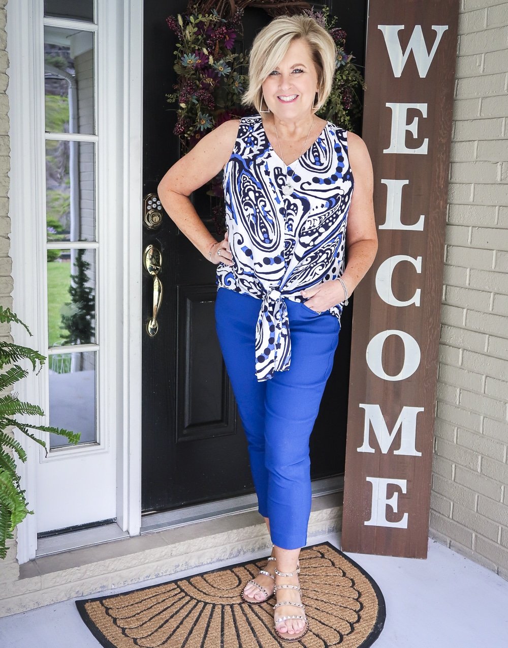Fashion Blogger 50 Is Not Old wearing a bright cobalt blue paisley tie-front top and blue pants with tan sandals with spikes from Steve Madden