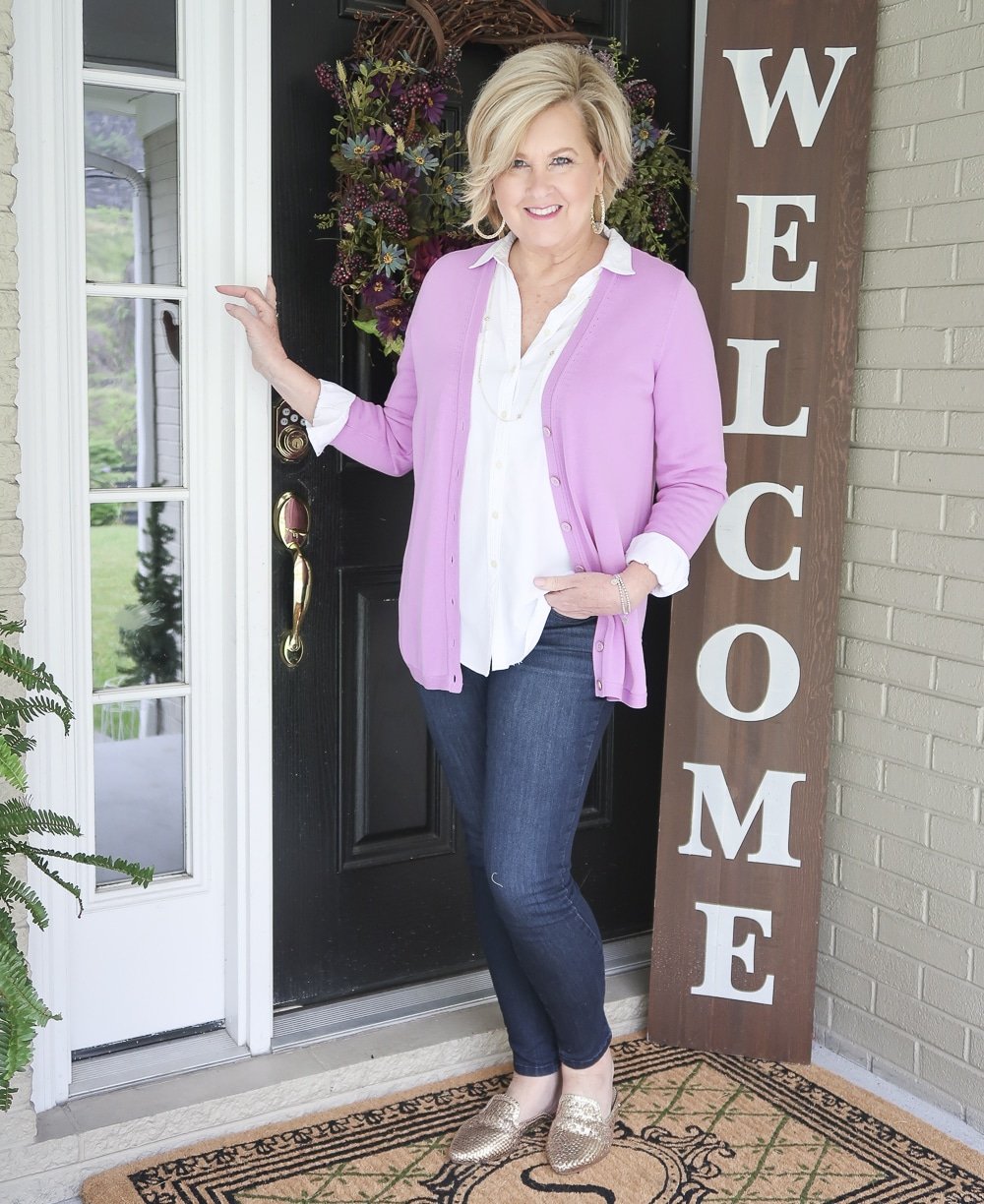 Fashion Blogger 50 Is Not Old is wearing a lilac cardigan over a white button down shirt with a pair of dark wash jeggings and gold mule shoes