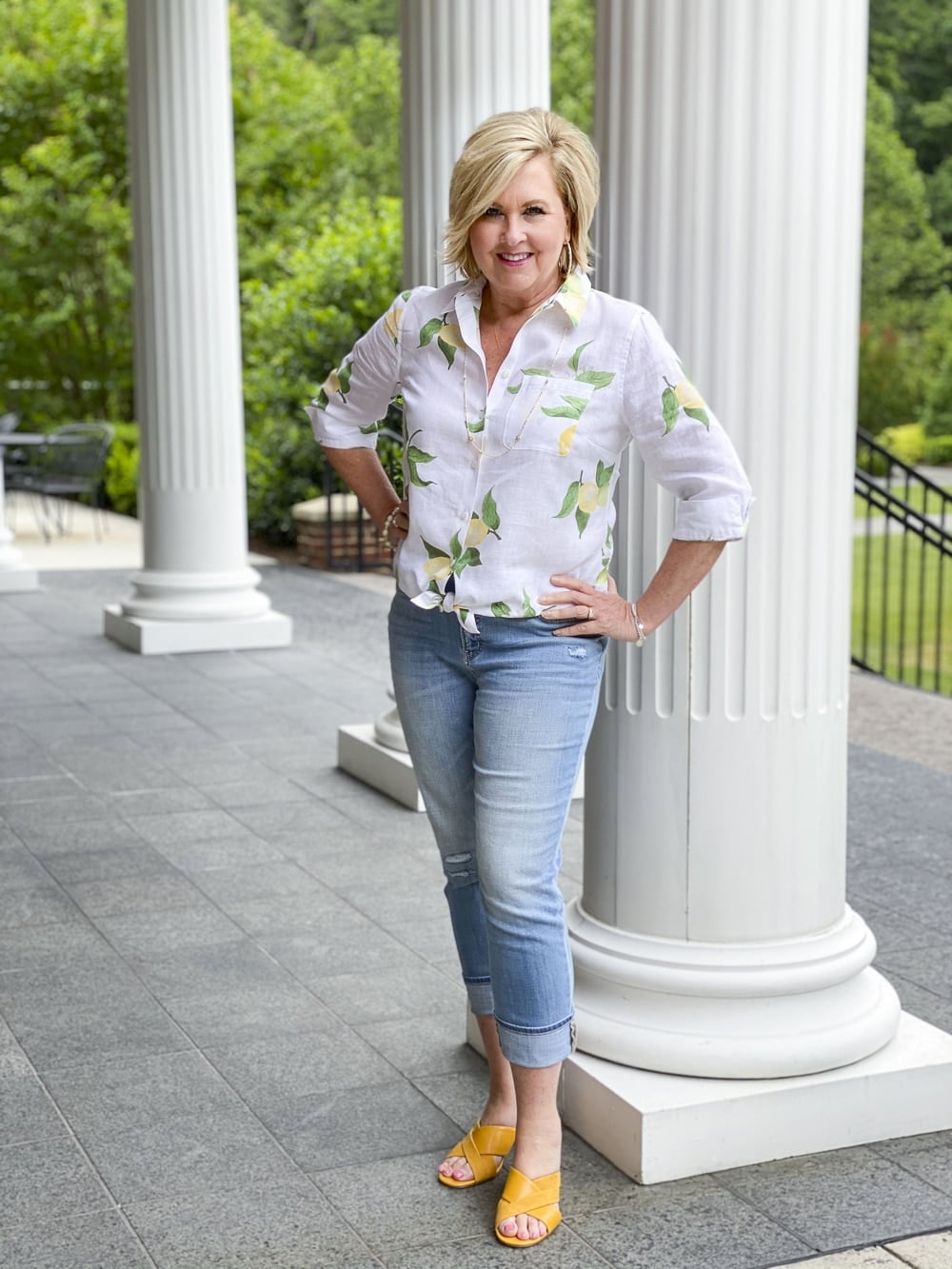 Fashion Blogger 50 Is Not Old is wearing a white button down shirt with yellow lemons, a pair of distressed girlfriend jeans, and mustard yellow block heel sandals