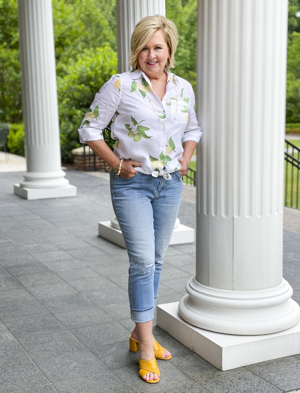 Fashion Blogger 50 Is Not Old is wearing a white button down shirt with lemons, a pair of distressed girlfriend jeans, and mustard yellow block heel sandals