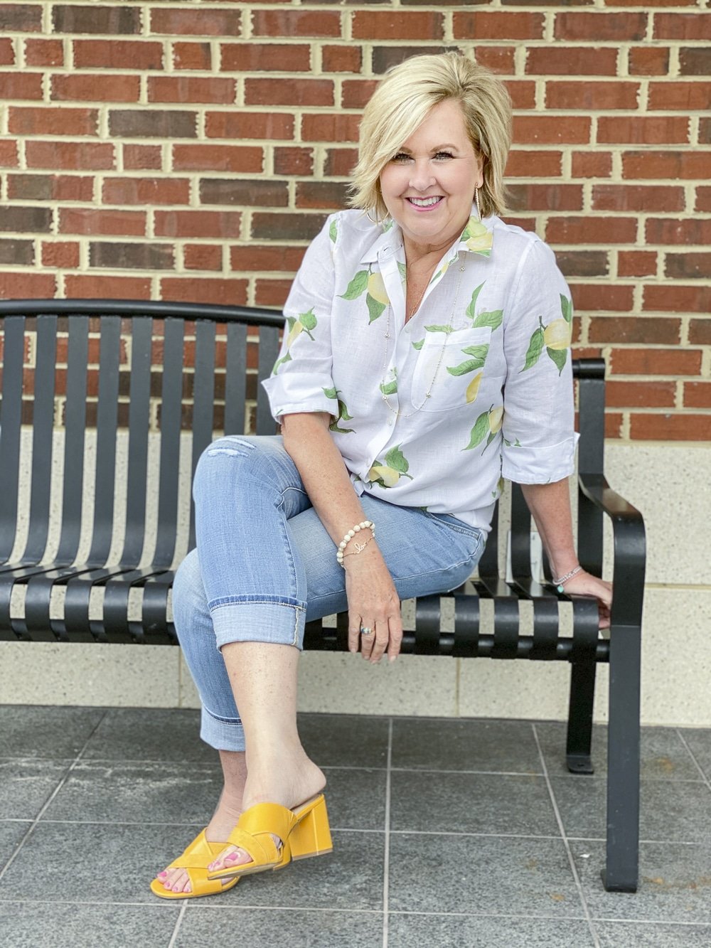 Fashion Blogger 50 Is Not Old is wearing a white button down shirt with yellow lemons, a pair of girlfriend jeans, and mustard yellow block heel sandals