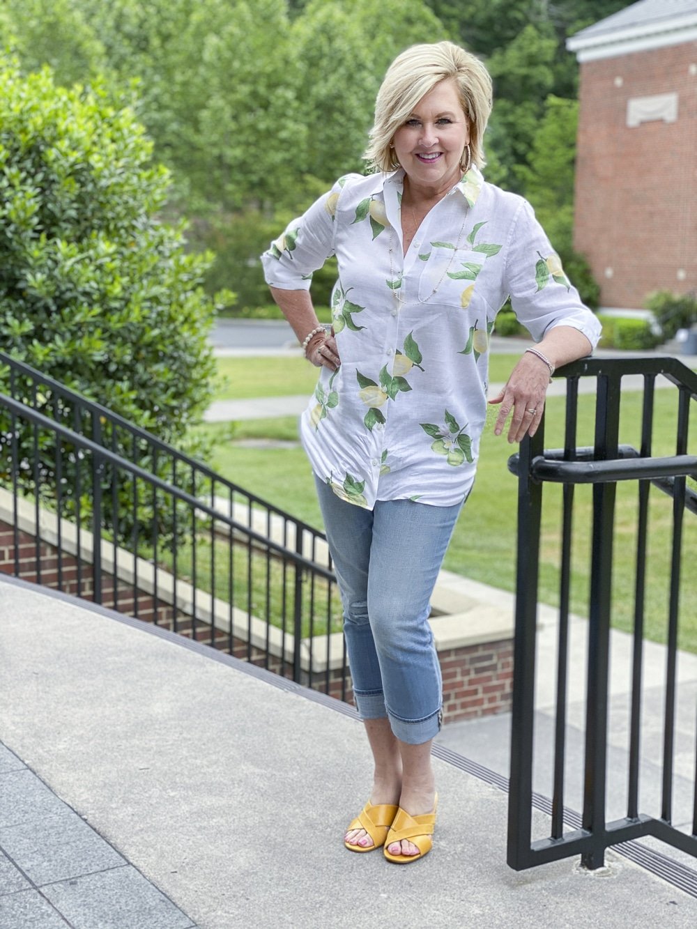 Fashion Blogger 50 Is Not Old is wearing a white shirt with yellow lemons, a pair of distressed girlfriend jeans, and mustard yellow block heel sandals