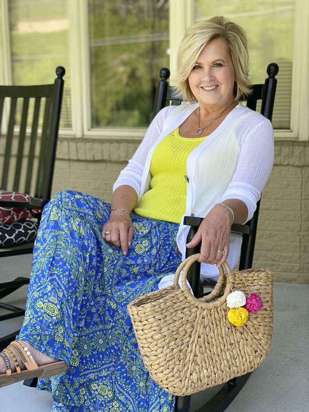 Fashion Blogger 50 Is Not Old is wearing styles from Walmart. A long white cardigan, a lemon yellow sweater tank top, a bright blue tiered skirt, embellished sandals, and a straw handbag