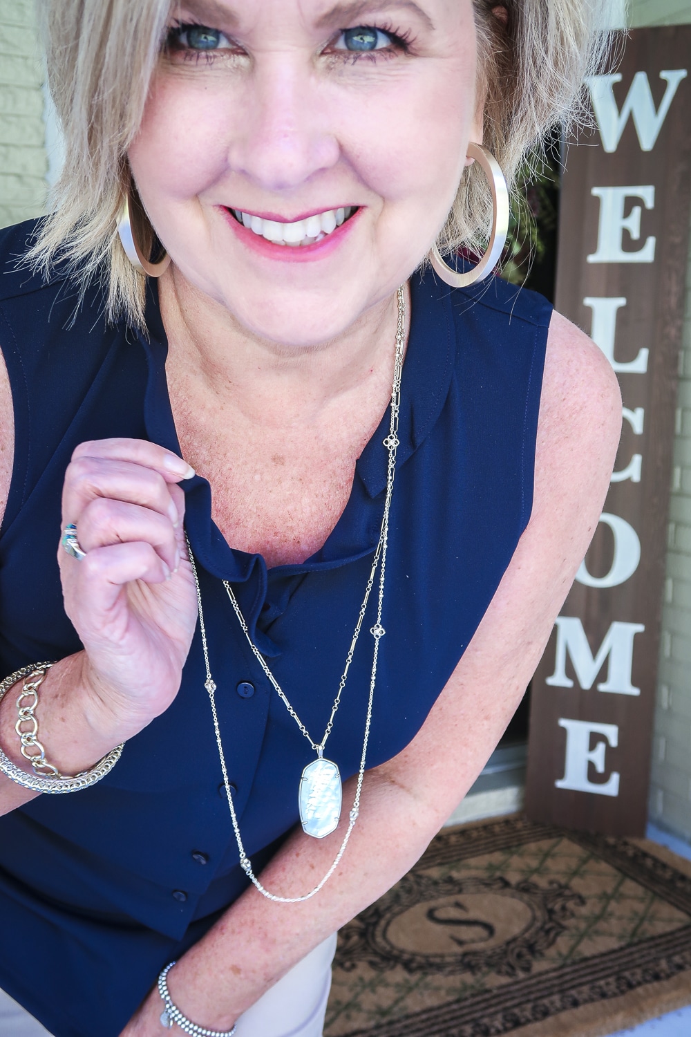 Fashion Blogger 50 Is Not Old is wearing a sleeveless blue top with a ruffled neckline and gold jewelry from Kendra Scott