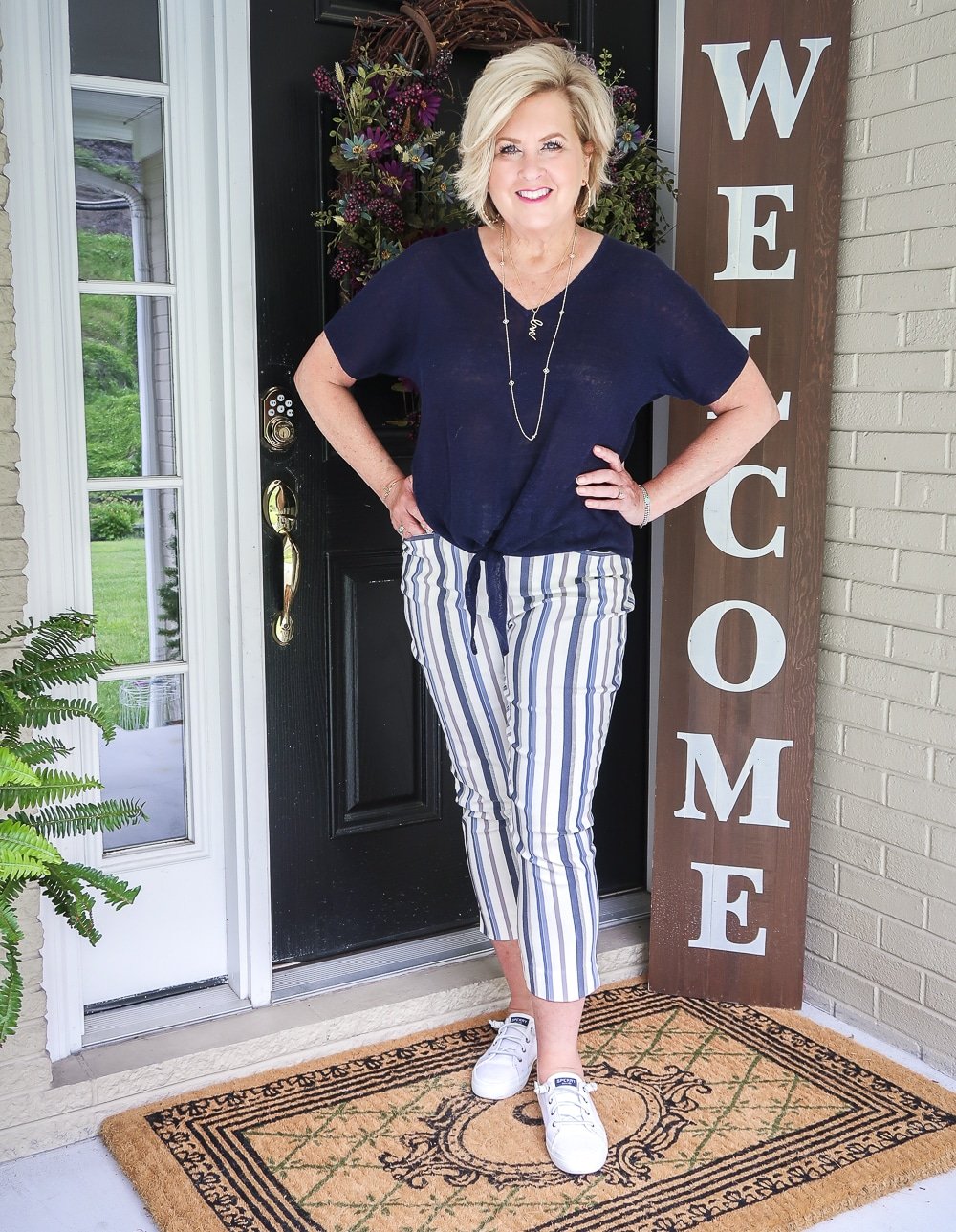 Fashion Blogger 50 Is Not Old is wearing a navy tie front top with striped crop pants and slip on sneakers
