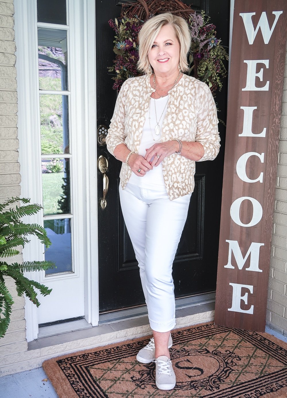 Fashion Blogger 50 Is Not Old wearing an all white outfit with a neutral colored leopard print cardigan and slip on sneakers
