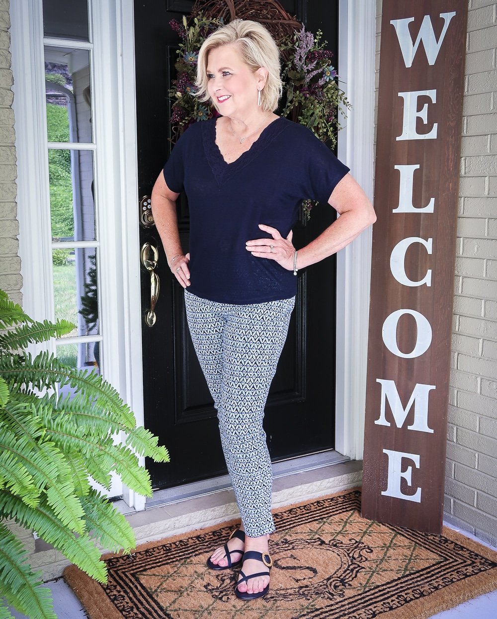 Fashion Blogger 50 Is Not Old is looking away and wearing a dark navy linen top with a lace neckline and printed ankle pants with navy sandals