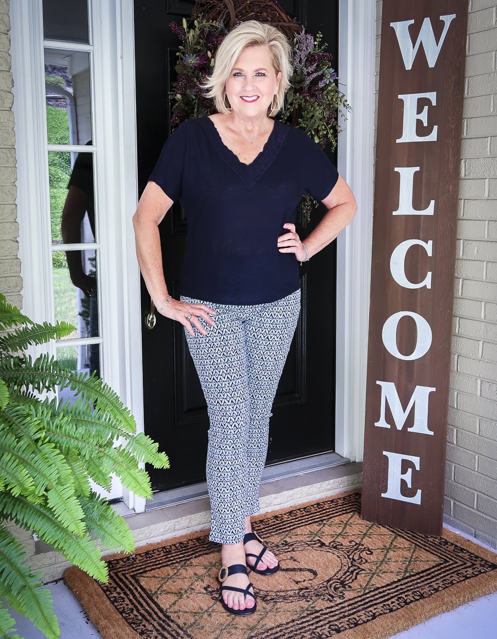 Fashion Blogger 50 Is Not Old wearing a navy linen top with a lace neckline and printed ankle pants with navy sandals