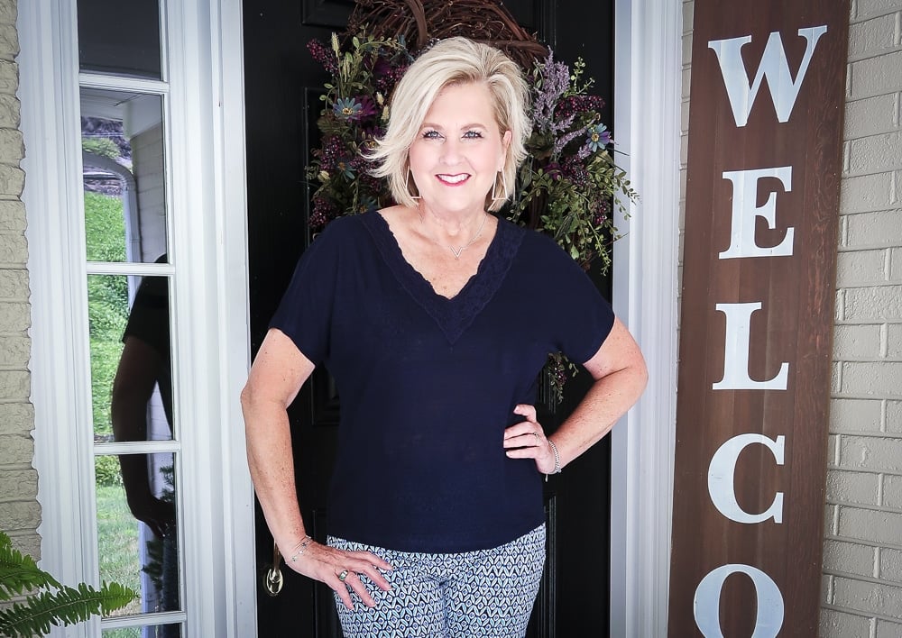 Fashion Blogger 50 Is Not Old wearing a navy top with a lace neckline and printed ankle pants with navy sandals