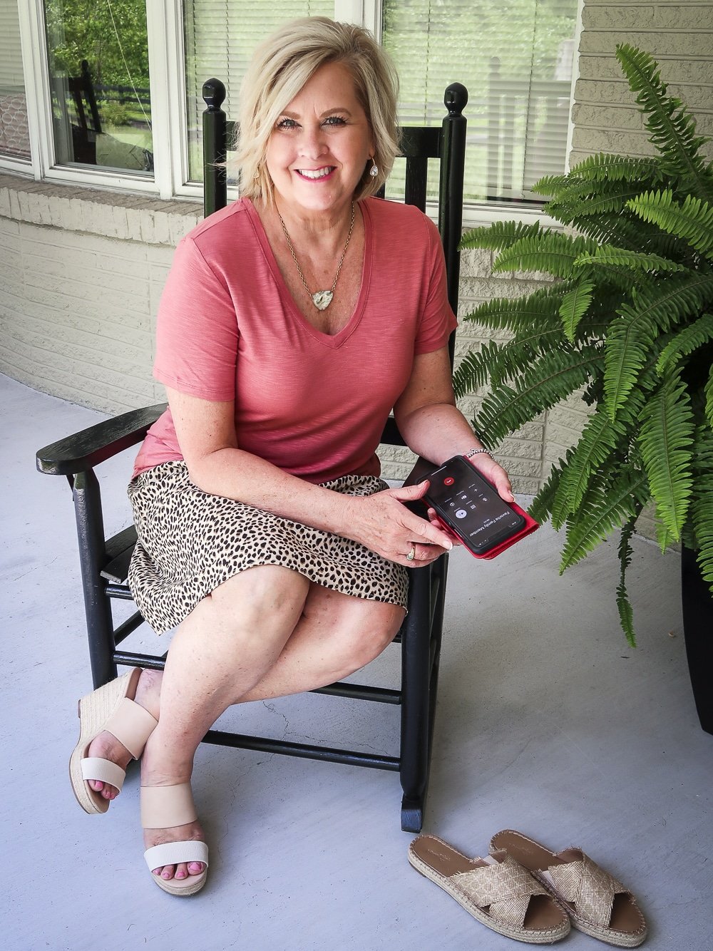 Fashion Blogger 50 Is Not Old is sitting in a rocking chair with a spice colored t-shirt with a leopard mini skirt and espadrille shoes
