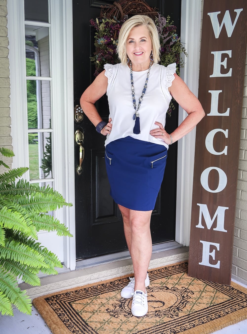 Fashion Blogger 50 Is Not Old is wearing an eyelet flutter sleeve top with a navy skort with zippers and a pair of white Sperry no-tie sneakers