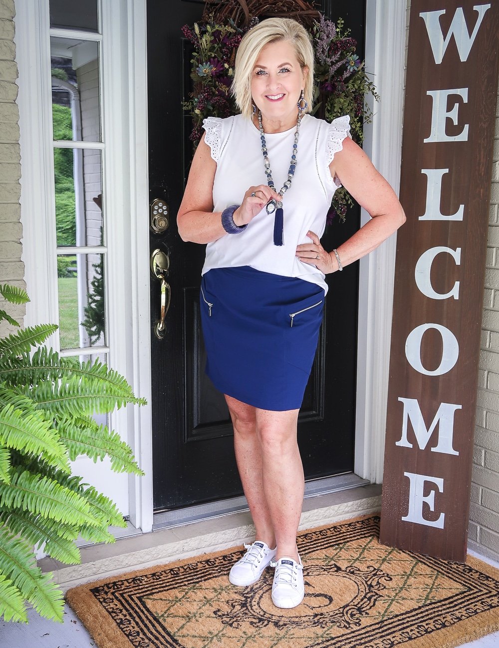 Fashion Blogger 50 Is Not Old is wearing an eyelet flutter sleeve top with a navy skort with silver zippers and a pair of Sperry no-tie sneakers
