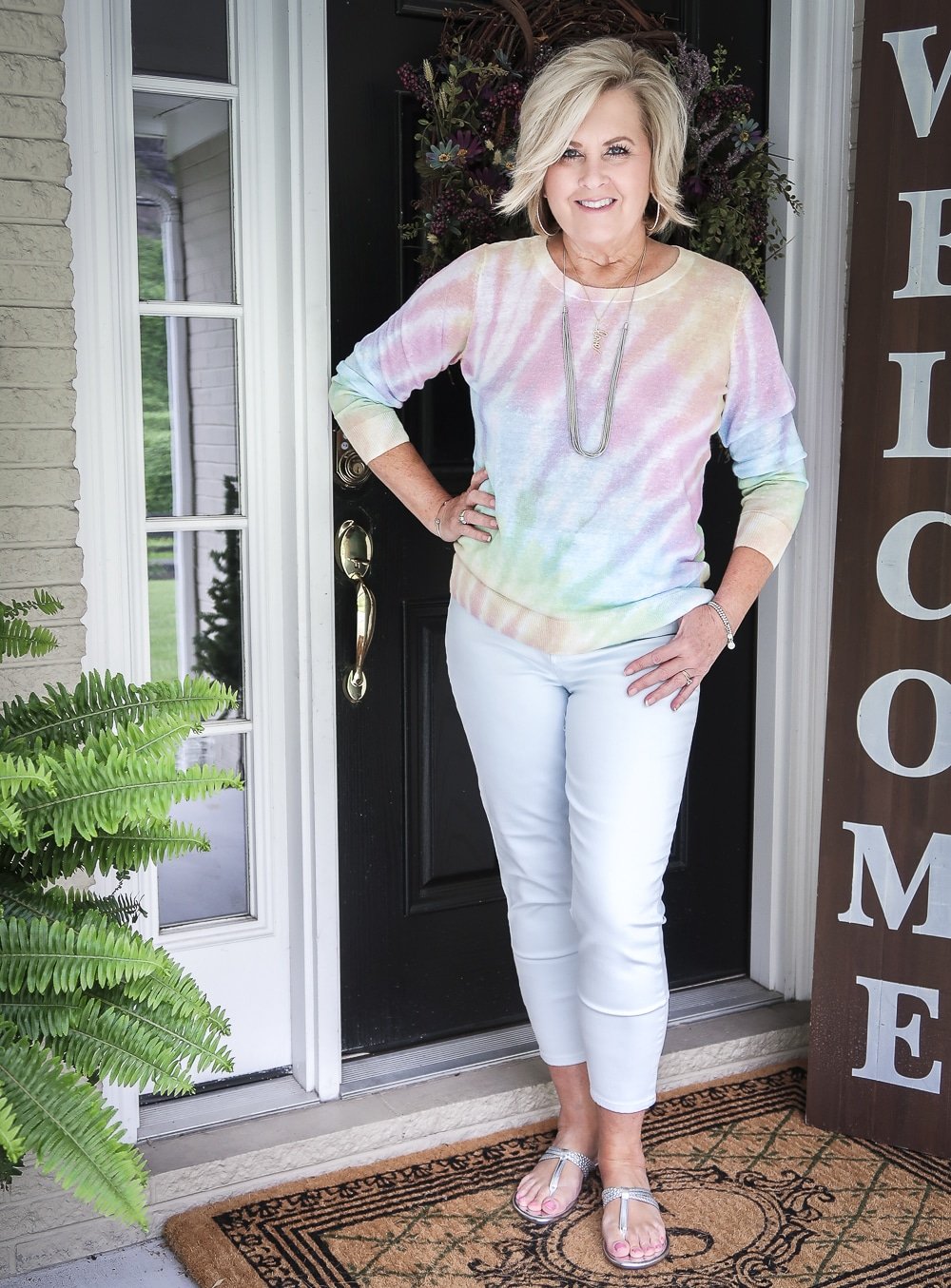 Fashion Blogger 50 Is Not Old is wearing a gorgeous tie-dye sweater with pale blue jeggings and silver braided sandals