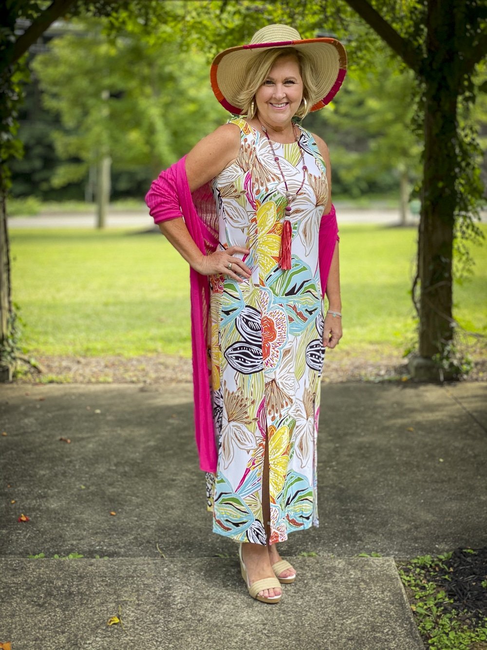 Fashion Blogger 50 Is Not Old is wearing a tropical print sleeveless dress, a pink cardigan, colorful accessories and white espadrilles