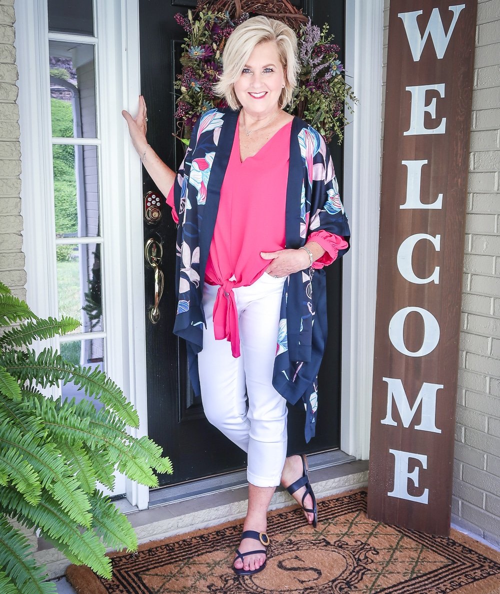 Fashion Blogger 50 Is Not Old is bright and colorful in a tie-front pink blouse, white girlfriend crop jeans, floral navy ruana, and navy sandals