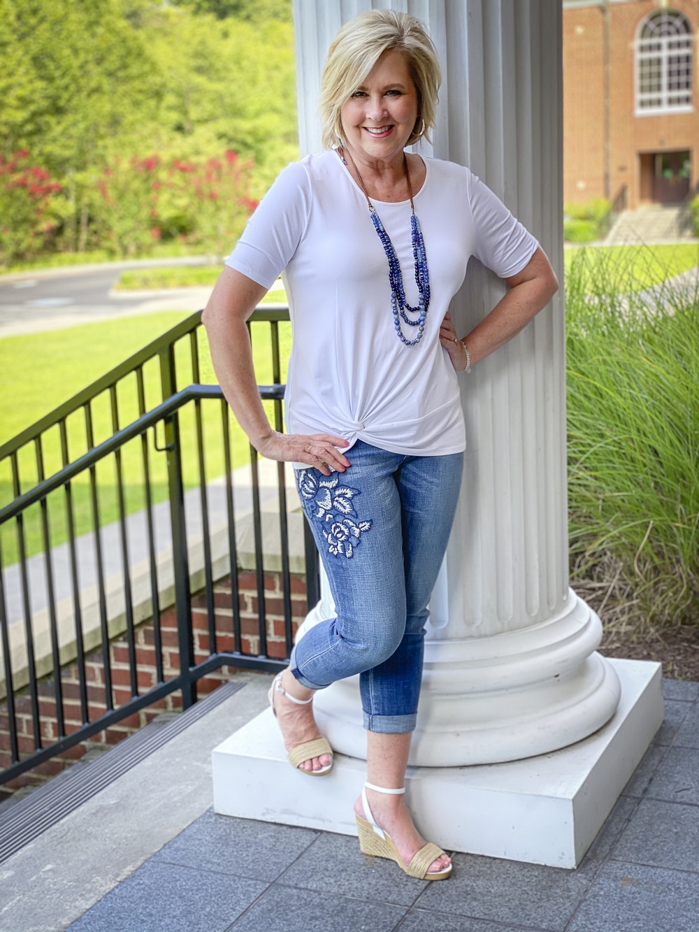 Fashion Blogger 50 Is Not Old is wearing a white twist top, embroidered jeans, and blue beaded jewelry