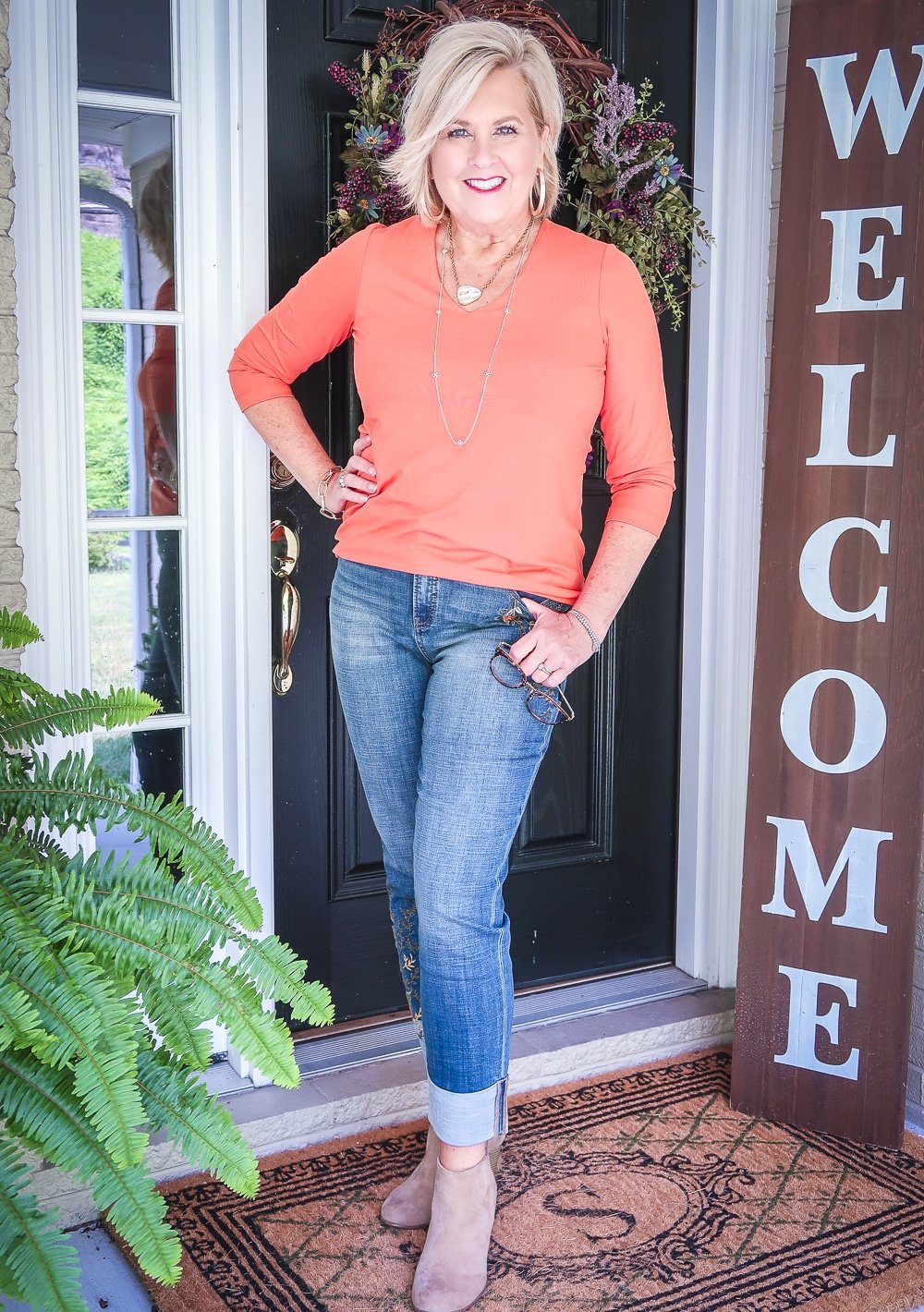 Fashion Blogger 50 Is Not Old is wearing a rust orange v-neck top, embroidered girlfriend jeans with a large cuff, and ankle boots