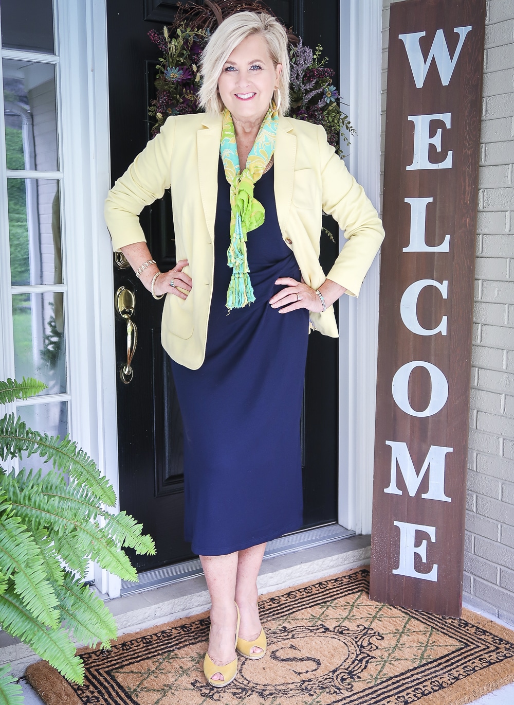 Fashion Blogger 50 Is Not Old is wearing a navy midi dress in all of the seasons. In the spring of the year, she added a pale lemon yellow blazer, a bright scarf, and a pair of yellow espadrille wedge shoes