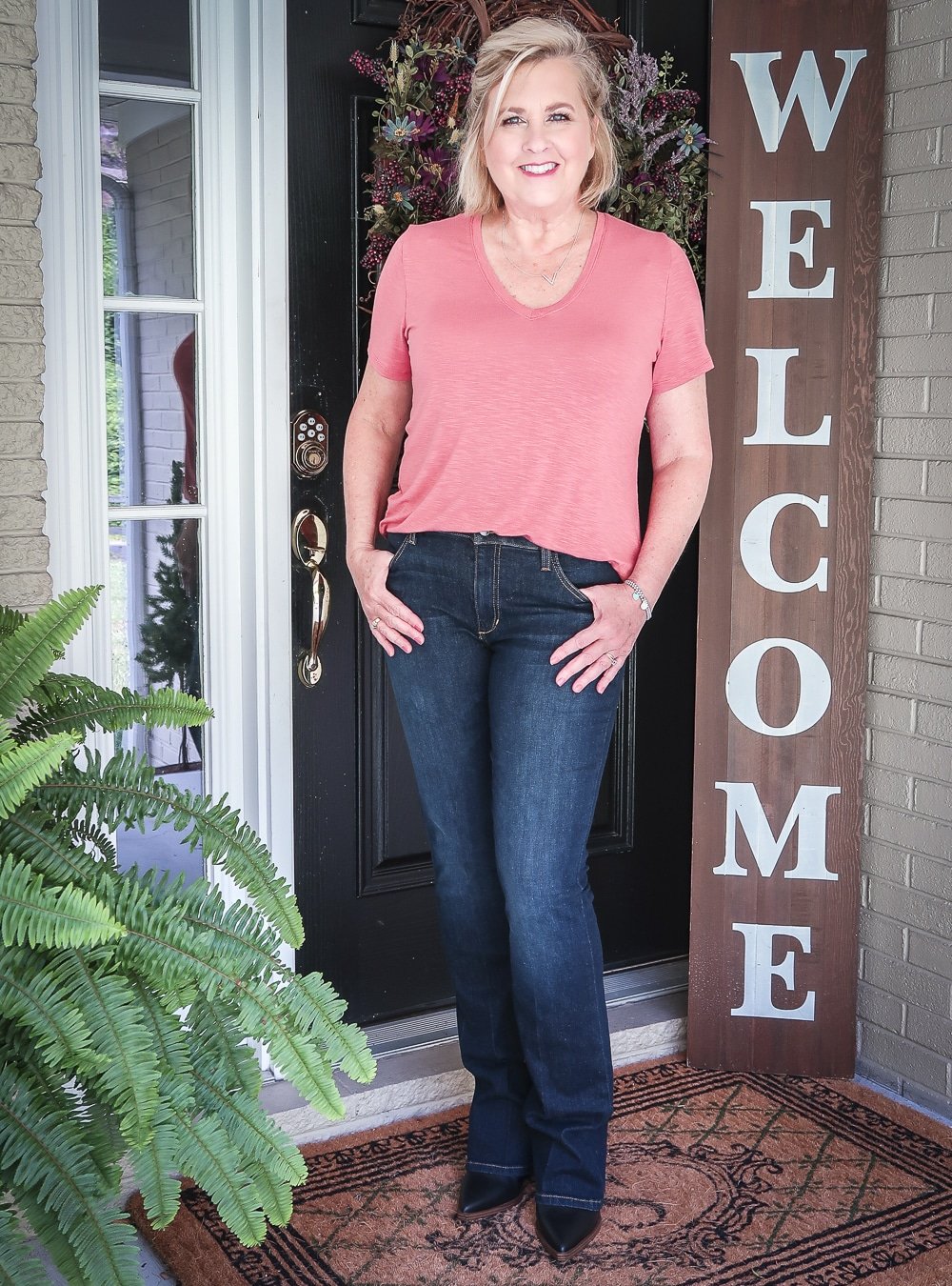 Fashion Blogger 50 Is Not Old is wearing a faded red v-neck t-shirt with a pair of dark bootcut jeans and black ankle boots