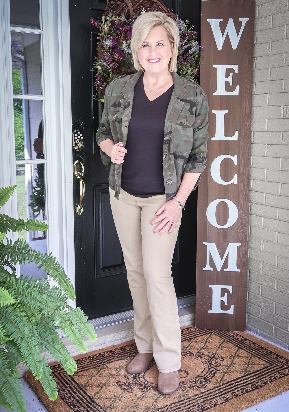 Fashion Blogger 50 Is Not Old is transitioning to fall in a black v-neck tank top, a olive green camo jacket, beige bootcut jeans, and brown ankle booties all from Walmart