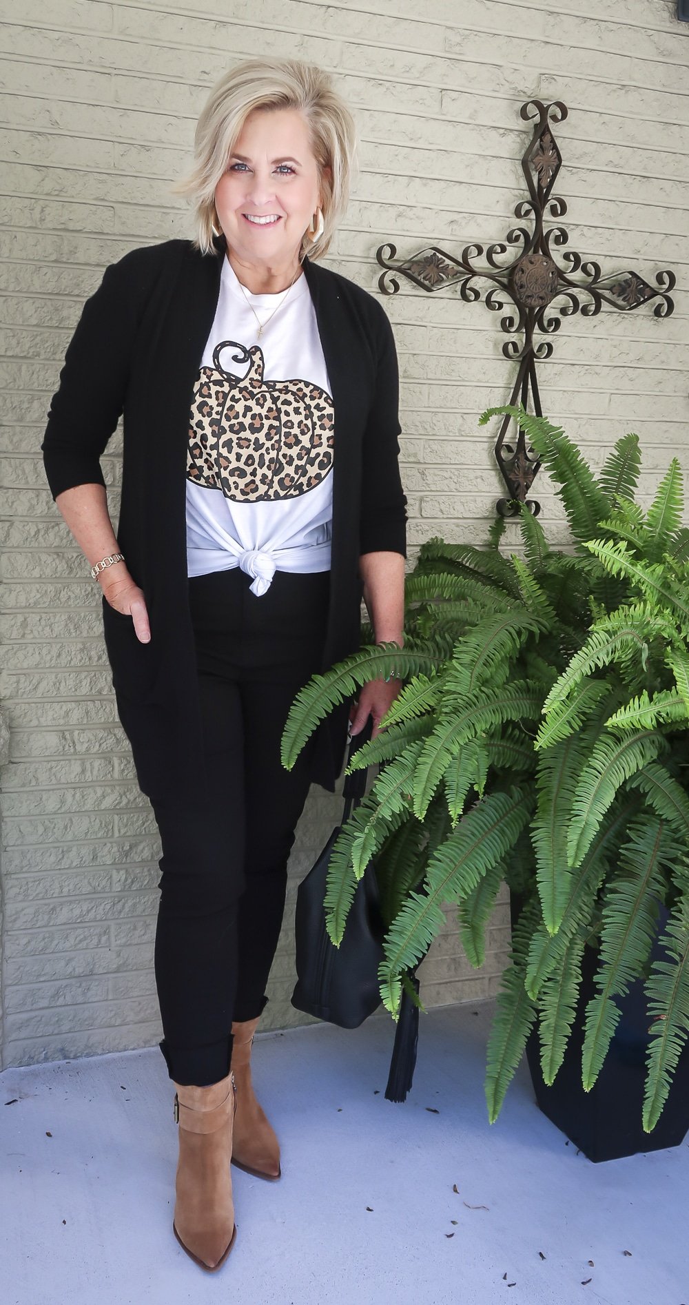 Fashion Blogger 50 Is Not Old is wearing a leopard print pumpkin t-shirt with a long black cardigan, black skinny jeans, carrying a black leather handbag, and wearing brown ankle boots