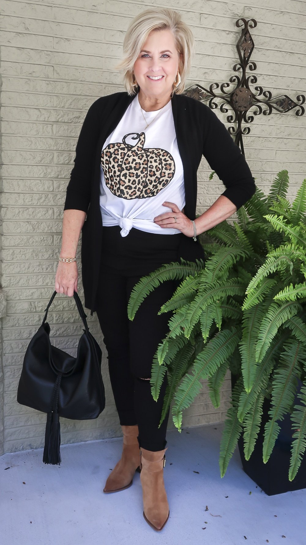 Fashion Blogger 50 Is Not Old is wearing a leopard print pumpkin t-shirt with a long black cardigan, black skinny jeans, carrying a black leather handbag, and wearing brown ankle booties