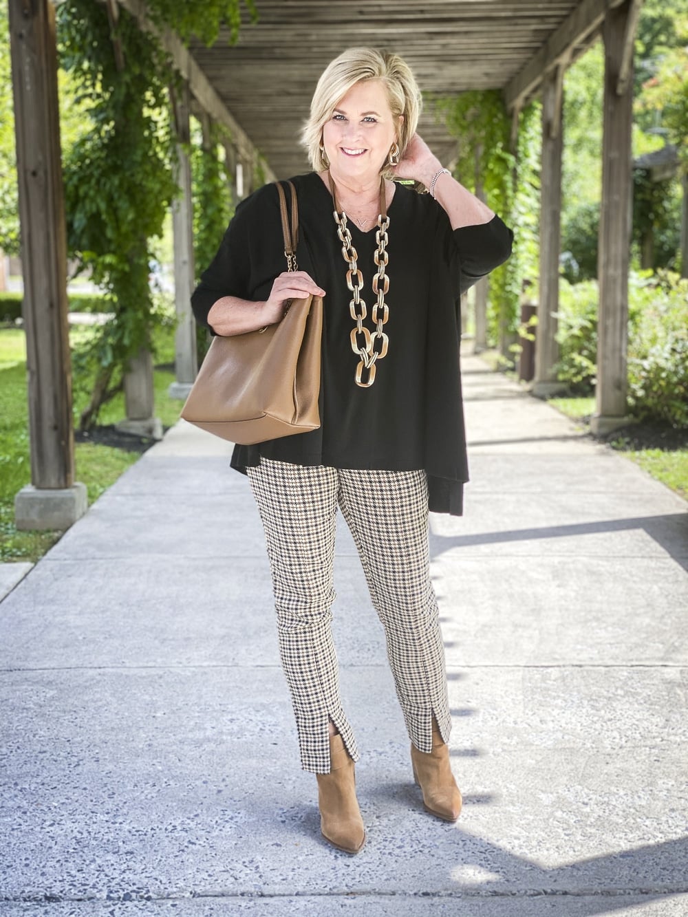Fashion Blogger 50 Is Not Old is wearing plaid pants in the fall with a black poncho, a brown leather handbag, and taupe ankle boots