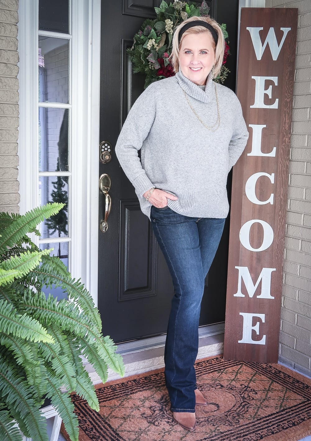 Fashion Blogger 50 Is Not Old has her hair pulled back in a headband, and wearing a chunky sweater, bootcut jeans, and ankle boots for fall