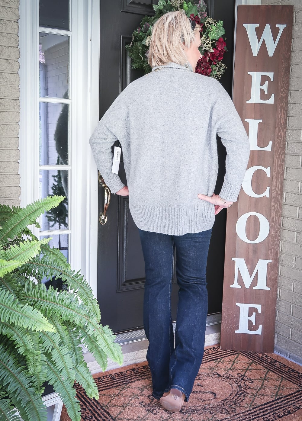 Fashion Blogger 50 Is Not Old has her back to us, and wearing a chunky sweater, bootcut jeans, and ankle boots for fall