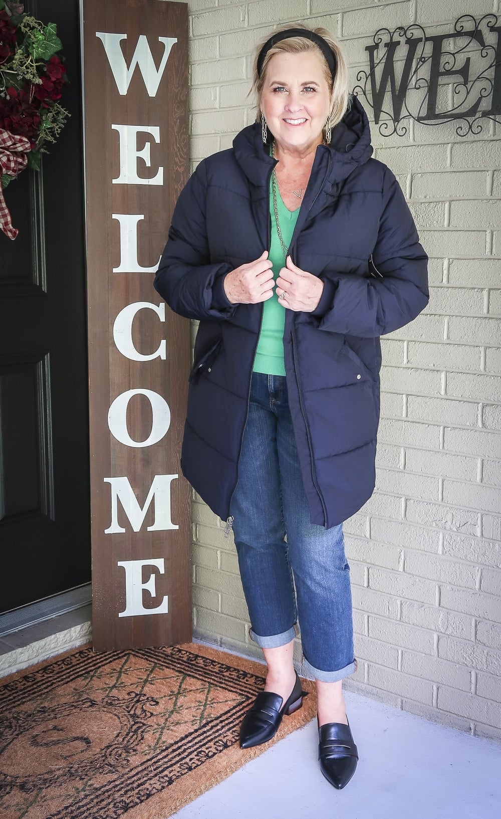 Fashion Blogger 50 Is Not Old is wearing a vibrant green v-neck sweater with a navy puffer coat, girlfriend crop jeans, and black pointy loafers